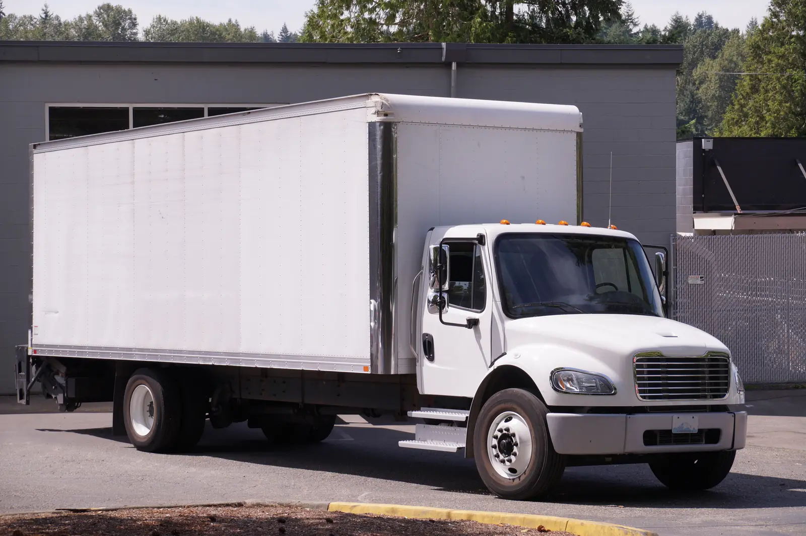 White box truck parked beside an industrial building.
