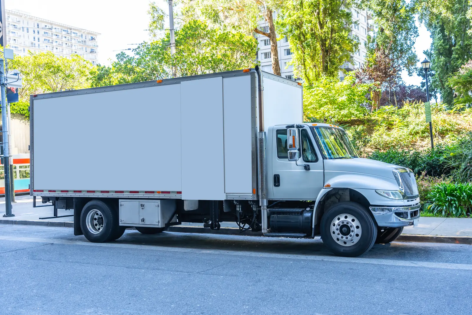 A light-colored box truck parked along a tree-lined street.